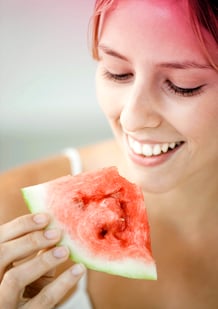 Bilde av en ung kvinne som spiser vannmelon. Bildet viser en av tipsene for å lindre menstruasjonssmerter - spis frukt eller grønnsaker som inneholder mye vann.