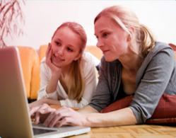 Bilde av mor og datter som bruker en PC sammen. Bildet viser viktigheten av kommunikasjon og å hjelpe datteren din finne den riktige informasjonen.